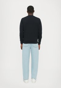 Zwarte sweatshirt met een ronde hals, ribgebreide manchetten en zoom; gecombineerd met lichtblauwe jeans en witte sneakers. Gezicht vanaf de achterkant.