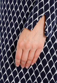 Marineblaue Stoff mit einem weißen Diamantmuster. Eine Hand ruht auf der strukturierten Oberfläche, die ein kontrastierendes geometrisches Design aufweist.