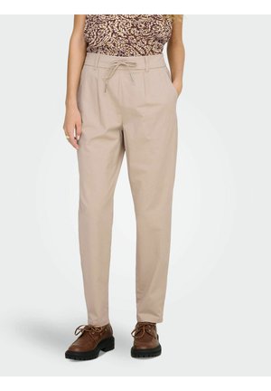 Femme portant un pantalon beige taille haute avec un nœud à l'avant et des poches, associé à des chaussures marron à lacets et un haut à motifs rentré.