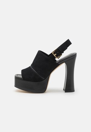 Sort ruskind plateau sandal med høj hæl med bred frontstrop og justerbar ankelrem med guldspænde på en udvidet hæl.