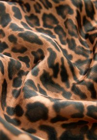 Látka s leopardím vzorom na pieskovom pozadí a čiernymi škvrnami, s hladkým, lesklým povrchom, ktorý vytvára plynulý vzhľad.