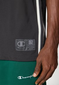 Close-up of a person wearing black and green Champion athleticwear with visible logos and labels on the shirt and shorts.