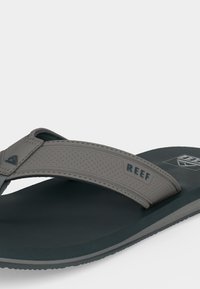 Γκρί και σκουροπράσινα σαγιονάρες Reef με διάτρητο λουράκι και μαλακή σόλα σε λευκό φόντο.