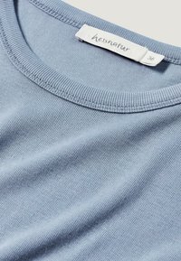 Ljusblå bomullströja med rund halsringning, ribbad struktur och en etikett som visar "hessnatur" samt storlek 36 på den inre kragen.