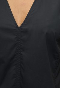 Κοντινή λήψη μαύρου ρούχου με V-λαιμόκοψη, ορατή κεντρική ραφή και μερικό δέρμα στο λαιμό.