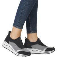 Black athletic shoes with mesh upper, silver accents, side zipper closure, and white platform soles. Worn with dark denim pants.