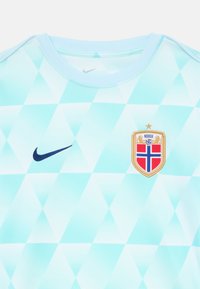 Svijetloplavi nogometni dres s geometrijskim dijamantnim uzorkom, Nike logo u tamnoplavoj boji i norveška stara s zlatnim akcentima.