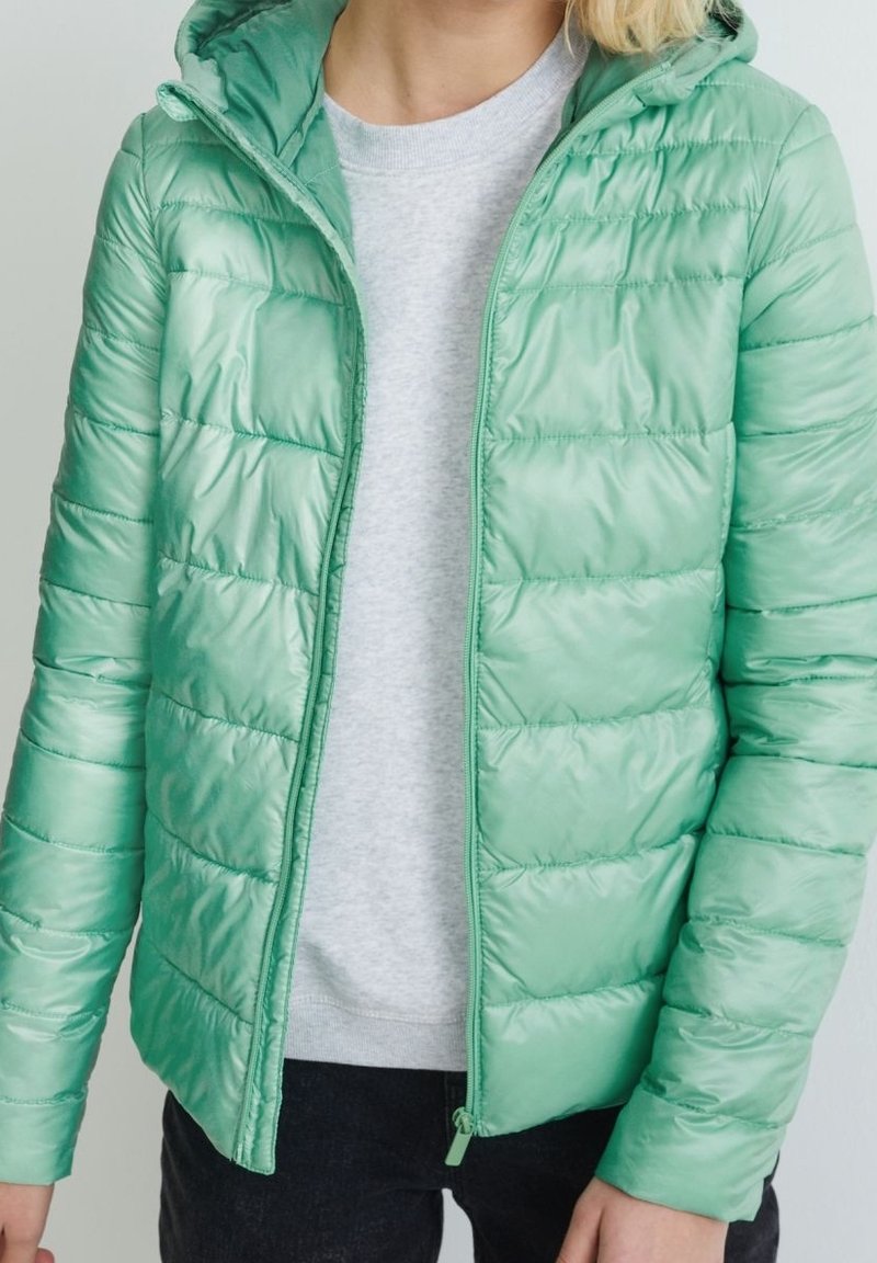 Chaqueta acolchada verde claro con capucha, que presenta una textura brillante, acolchado horizontal y cierre de cremallera. Lleva puesta una sudadera gris debajo.