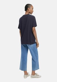 Navyblaue Baumwoll-T-Shirt mit lockerer Passform, kombiniert mit hellblauen weiten Jeans und cremefarbenen Schnürschuhen. Einfaches Design und lässiger Stil.