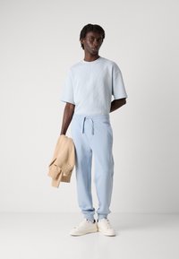 Lyseblå kortermet ribbestrikket T-skjorte kombinert med matchende joggebukser, holder en beige hettegenser, fullført med hvite sneakers.