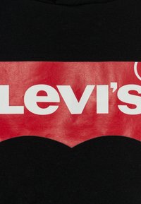 Czarna bawełniana koszulka z dużym czerwonym logo Levi's z białym napisem i zaokrąglonym dołem, tworząca wyrazisty graficzny kontrast.