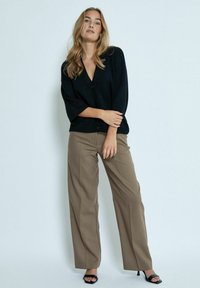 Cardigan noir à boutons avec des manches trois-quarts, associé à un pantalon large beige et des sandales à talons noires. Tissu lisse, coupe décontractée.
