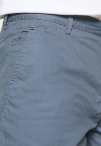 Pantalones de tela azul claro con una superficie texturada, que presentan un diseño ajustado, bolsillos laterales y detalles de costura sutiles.