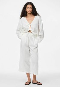 Ensemble en coton blanc composé d'un haut court à manches longues avec un devant noué et d'un pantalon à jambes larges avec une taille élastique.