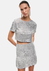 Zilveren sequinen crop top en rok set, met een aansluitend ontwerp, korte mouwen en een gerimpelde zoom op de rok. Glad textuur.