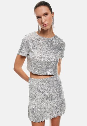 Zilveren sequinen crop top en rok set, met een aansluitend ontwerp, korte mouwen en een gerimpelde zoom op de rok. Glad textuur.