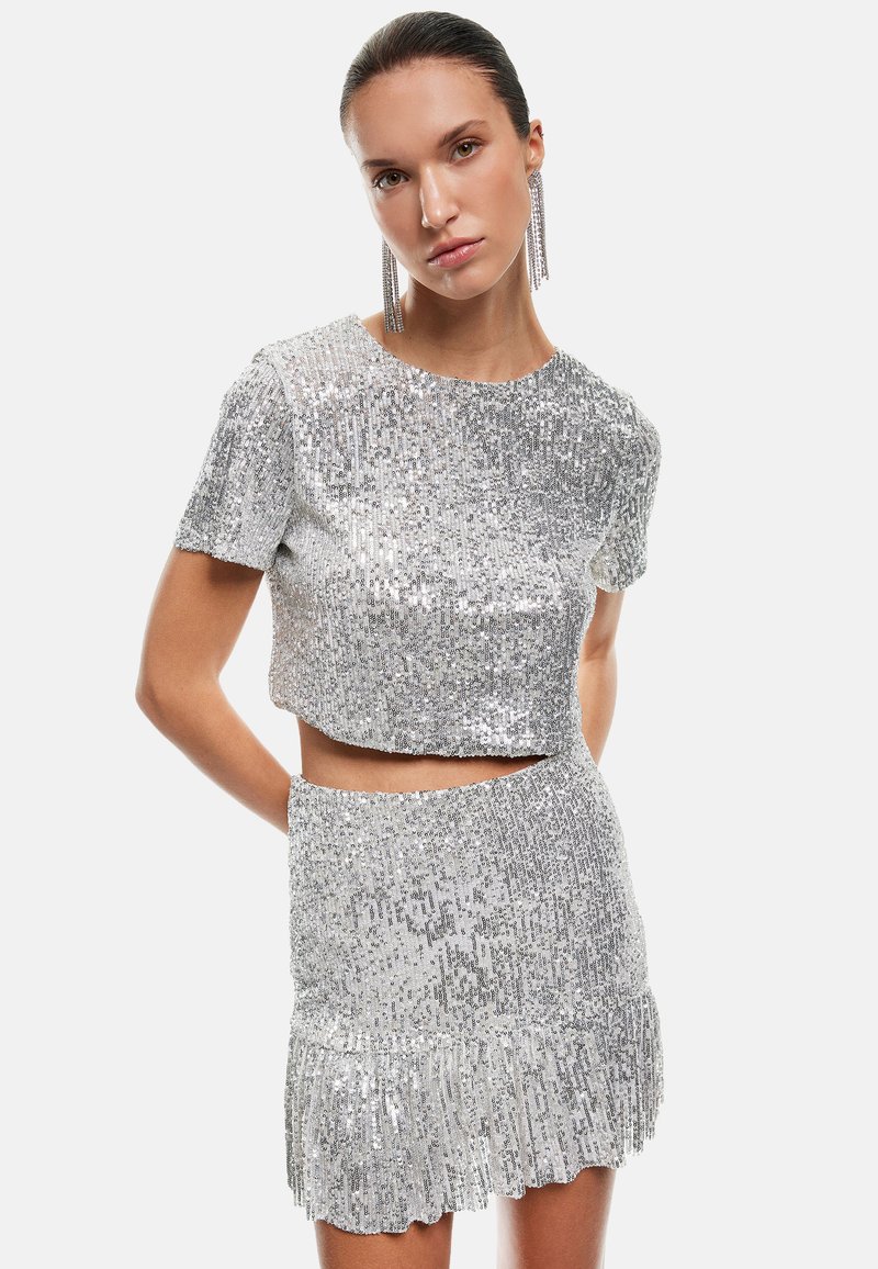 Zilveren sequinen crop top en rok set, met een aansluitend ontwerp, korte mouwen en een gerimpelde zoom op de rok. Glad textuur.