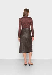 Top a maniche lunghe, a fantasia in rosso e nero, abbinato a una gonna midi in pelle marrone. La gonna presenta una vita aderente e tasche visibili.