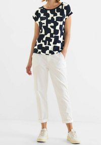 Marinblå och vit mönstrad t-shirt med avslappnad passform, korta ärmar, rund halsringning, kombinerad med vita, löst sittande byxor och krämfärgade sneakers.