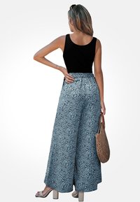 Top negro de tirantes combinado con pantalones de pierna amplia en azul claro con un patrón salpicado de negro. Acabado con un bolso de mimbre y sandalias en tonos neutros.