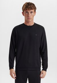 Sort langærmet sweatshirt med V-hals og ribbede manchetter. Har et rundt logo-patch på brystet; lavet af blødt stof.