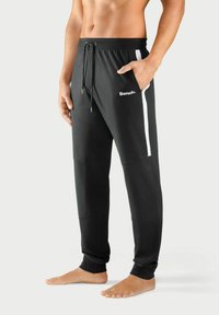 Schwarze Sporthosen aus weichem Stoff mit elastischem Bund, Kordelzug, Seitentaschen und weißen Streifen an den Seiten.