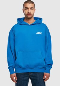 Kék kapucnis pulóver elülső zsebbel, bal oldalon fehér logóval. Puha, textúrált anyagból készült. Lazán illeszkedő fazon.