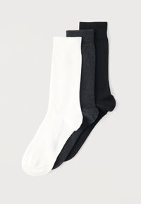 Τρία ζευγάρια διπλωμένων κάλτσες μέσης σε άσπρο, σκούρο γκρι και μαύρο, τοποθετημένα στρωματοποιημένα σε ανοιχτό φόντο.