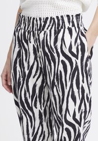 I pantaloni a righe bianche e nere presentano una cintura elastica, tasche laterali e un tessuto leggero con un design testurizzato e fluente.