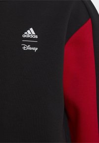 Black sweatshirt with red accents, featuring a textured fabric. Includes white Adidas and Disney logos on the front.