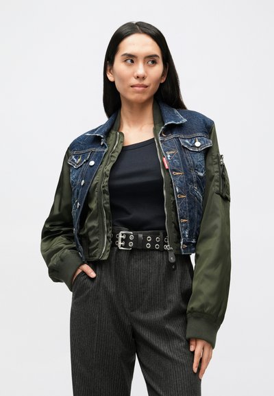 Korte jas die denim en olijfgroene stof combineert. Heeft een voorzijde met knopen, zakken en een geribbelde zoom. Gecombineerd met een donker topje en gestreepte broek.