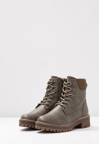 Bottines en cuir vert olive avec des accents en suède marron, dotées d'œillets en métal, de lacets et de semelles en caoutchouc robustes pour une meilleure adhérence.