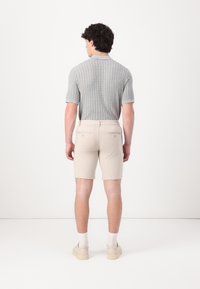 Polo tricotat de culoare gri deschis cu mâneci scurte, asortat cu pantaloni scurți bej cu buzunare pe spate. Modelul poartă adidași crema și șosete albe.
