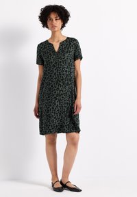 Robe verte à manches courtes avec un motif léopard, un décolleté en V et une coupe décontractée, fabriquée dans un tissu lisse. Ballerines noires.