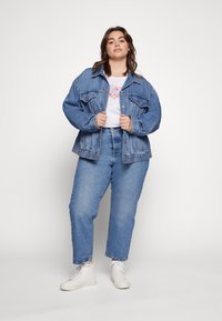 Veste en denim bleu clair avec une coupe décontractée, deux poches poitrine et des boutons à l'avant. Associée à un jean bleu taille haute et des baskets blanches.