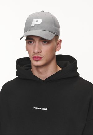 Grå baseballcap med en hvit 'P' logo, parret med en svart hettegenser som har teksten "PEGADOR" i hvitt.