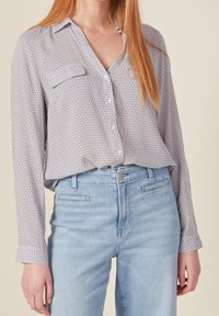 Lekka koszula z guzikami w niebiesko-białym kolorze, z geometrycznym wzorem, dwoma kieszeniami na piersi i długimi rękawami, w komplecie z jasnymi dżinsami.