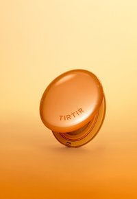 Pomarańczowe kompaktowe opakowanie na podkład z brandingiem "TIRTIR" częściowo otwarte na tle w pasującym pomarańczowym gradiencie.