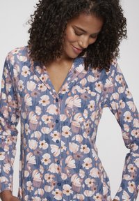Kvetinová košeľa s button-up zapínaním v modrej farbe s ružovým a bielym vzorom kvetov, s dlhými rukávmi a náprsnom vreckom. Mäkka textúra látky.