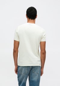 Ελαφρύ μπεζ κοντομάνικο μπλουζάκι από απαλό ύφασμα, στρογγυλή λαιμόκοψη, κανονική εφαρμογή, συνδυασμένο με ξεθωριασμένο μπλε τζιν. Μινιμαλιστικός σχεδιασμός, χωρίς εμφανή λογότυπα.