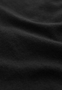 Gros plan d’un tissu noir lisse avec des plis souples et une surface légèrement texturée et mate.