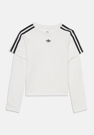 Hvit langermet lagdelt skjorte med svarte Adidas-striper på skuldrene og svart Adidas trefoil-logo på midten av brystet.
