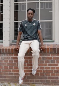 Jersey deportivo verde oscuro con rayas y logo blancos, combinado con pantalones color crema claro y zapatillas blancas con acentos rojos.