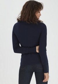 Maglione blu navy a maniche lunghe con design aderente, polsini e orlo a costine. La schiena del modello è rivolta verso l'obbiettivo, mostrando la texture liscia e la silhouette.