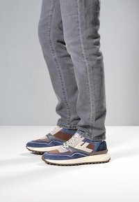 Sneakers med en kombination av blå mocka och bruna läderdetaljer, med en vit mellansula och ett mönstrat yttersula.