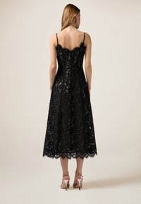 Schwarzes Spitzen-Midi-Kleid mit verstellbaren Spaghettiträgern, detaillierten Blumenmustern, Wellenkante und tailliertem Oberteil.