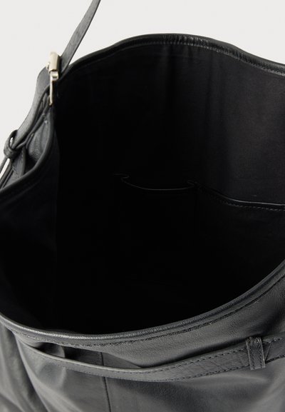 Μαύρη δερμάτινη τσάντα ώμου με ανοιχτό πάνω μέρος που αποκαλύπτει έναν ευρύχωρο εσωτερικό χώρο και δύο μικρές εσωτερικές τσέπες πάνω σε απλό φόντο.