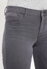 Gray denim jeans with a fitted design. Features a front pocket, zipper fly, and subtle texture. The waistband has belt loops.