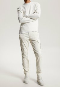 Vit stickad tröja kombinerad med beige cargobyxor med sidofickor, avslutad med vita sneakers. Slät textur och avslappnad passform.