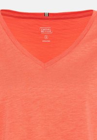 Koralfarvet V-hals t-shirt lavet af økologisk bomuld, med en struktureret overflade. Den indvendige halskant har et kontrasterende bånd med striber. Størrelse: S.